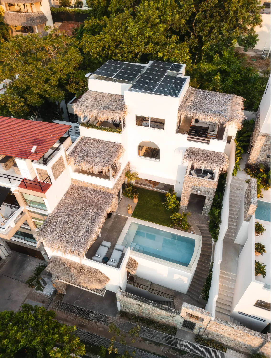 A white house with palapa roofs and a pool, from above